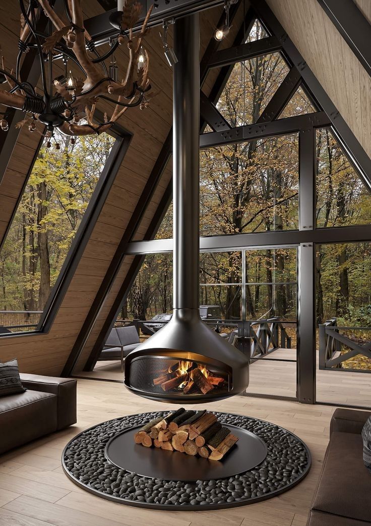 Nowoczesny kominek wiszący w salonie domu z dużymi przeszkleniami – widok na las, drewno opałowe i designerskie wnętrze z naturalnym światłem